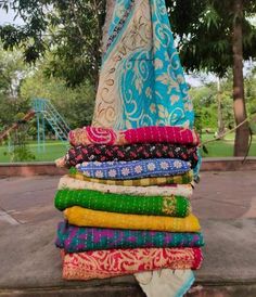 a stack of colorful scarves sitting on top of a cement floor next to a tree