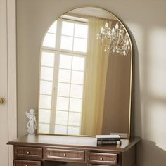 a large mirror sitting on top of a wooden dresser next to a window with a chandelier hanging from it