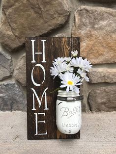 a mason jar with daisies in it sitting next to a sign that says home