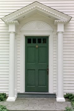 a green door is in front of a white house with pillars and columns on either side