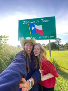 two girls are hugging under a welcome to texas sign in front of a grassy field