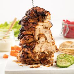 a large piece of meat sitting on top of a cutting board next to sliced cucumbers and crackers