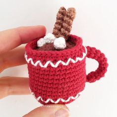 a crocheted coffee cup with marshmallows in it is being held by a hand