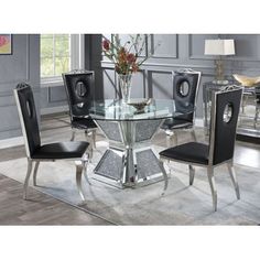 a glass dining table with black chairs and silver accents on the base is in front of a gray wall