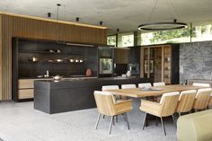 a dining room table and chairs in front of an open kitchen area with stone walls