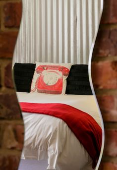 a red phone sitting on top of a white bed next to a brick wall in front of a mirror