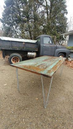 an old rusty table sitting in the middle of a dirt field next to a truck