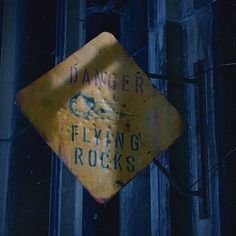 a yellow sign hanging from the side of a building that says danger flying rocks on it