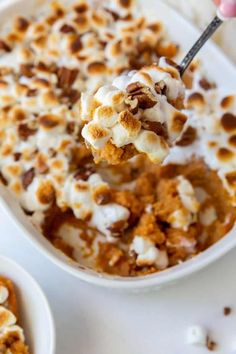 a spoon full of dessert with marshmallows and pecans in the bowl