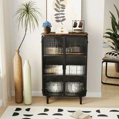 a black cabinet sitting next to a vase on top of a white and black rug