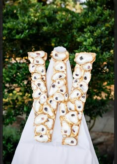 the letter w is made out of shells on a white table cloth with trees in the background