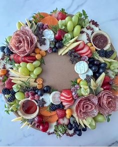 a fruit and vegetable wreath is displayed on a marble surface with grapes, strawberries, raspberries, melon, blueberries, blackberries