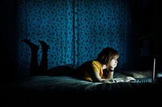 a woman laying on her bed in the dark using a laptop computer at night time