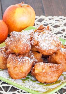 powdered sugar covered pastries on a green plate next to two oranges and an apple