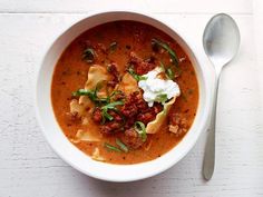 a white bowl filled with pasta and meat soup on top of a table next to a spoon