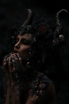 a woman with horns on her head and body covered in mud, holding her hands to her face