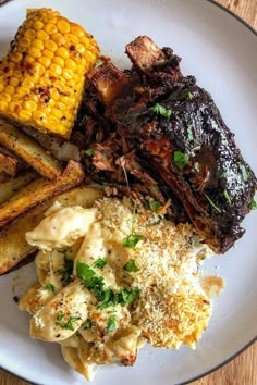 a white plate topped with meat, potatoes and corn on the cob covered in sauce