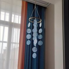 a wind chime hanging from the side of a window with curtains in the background