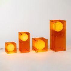 three orange lamps sitting next to each other on a white surface with one light turned yellow