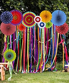 an assortment of colorful paper umbrellas hanging on a wall in the grass next to a picnic table