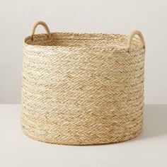 a large woven basket with handles on the bottom is shown in front of a white wall