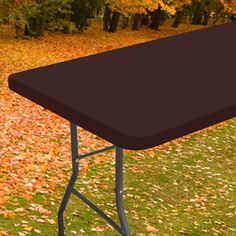 a black table sitting on top of a lush green field next to trees with yellow leaves