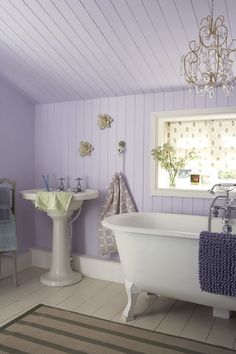 a white bath tub sitting under a window next to a sink in a purple bathroom