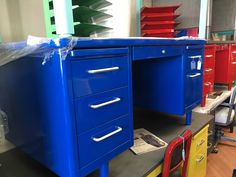 an office desk with several drawers and chairs in the background, all painted bright blue