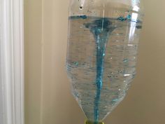 a large glass filled with water sitting on top of a wooden table next to a white wall