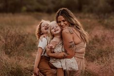 a mother and her two children are hugging in a field with tall brown grass on the ground