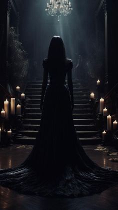 a woman in a long black dress standing at the bottom of stairs with candles around her