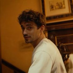 a man with curly hair is standing in front of a mirror and looking at the camera