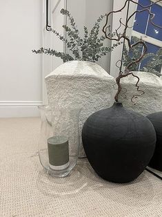 two black vases sitting on the floor next to each other with a plant in them