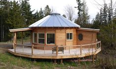 a round wooden structure with a metal roof in the middle of some trees and grass