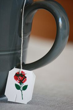 a coffee cup with a tag hanging from it's handle and a rose on the side