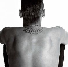 the back of a man with tattoos on his upper and lower back, standing in front of a white background