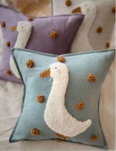 three decorative pillows on a bed with white and blue covers, one in the shape of a seagull