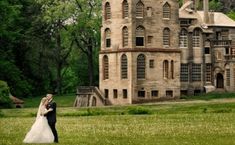 a bride and groom are standing in front of an old castle like building that is surrounded by trees