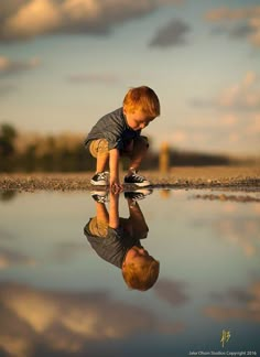 a young boy is playing in the water with his reflection on the ground and clouds