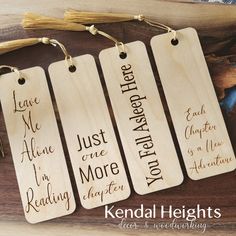 four wooden bookmarks with handwritten words on them, hanging from a wood table