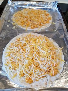 two uncooked pizzas sitting on top of an aluminum pan covered in cheese