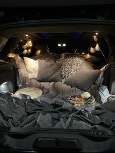 an open trunk filled with pillows and food on top of a bed in the back of a car