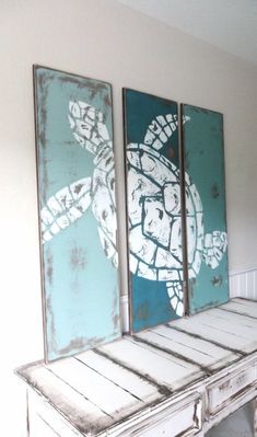 three sea turtle paintings are displayed on an old white table in the corner of a room