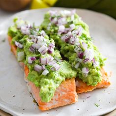 two pieces of salmon covered in guacamole and onions on a white plate