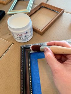 a person is holding a brush near some framed pictures and other art supplies on the table