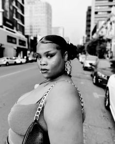 a black and white photo of a woman standing on the side of a road with cars behind her