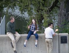 three people are sitting on a wall near the water and one person is holding a flower