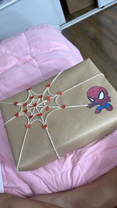 a gift wrapped in brown paper with spiderman on it sitting on top of a bed