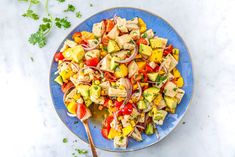 a blue plate topped with chicken and veggies next to a spoon on a white table