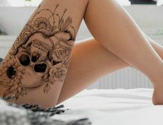 a woman's legs with tattoos and flowers on them, sitting on a bed